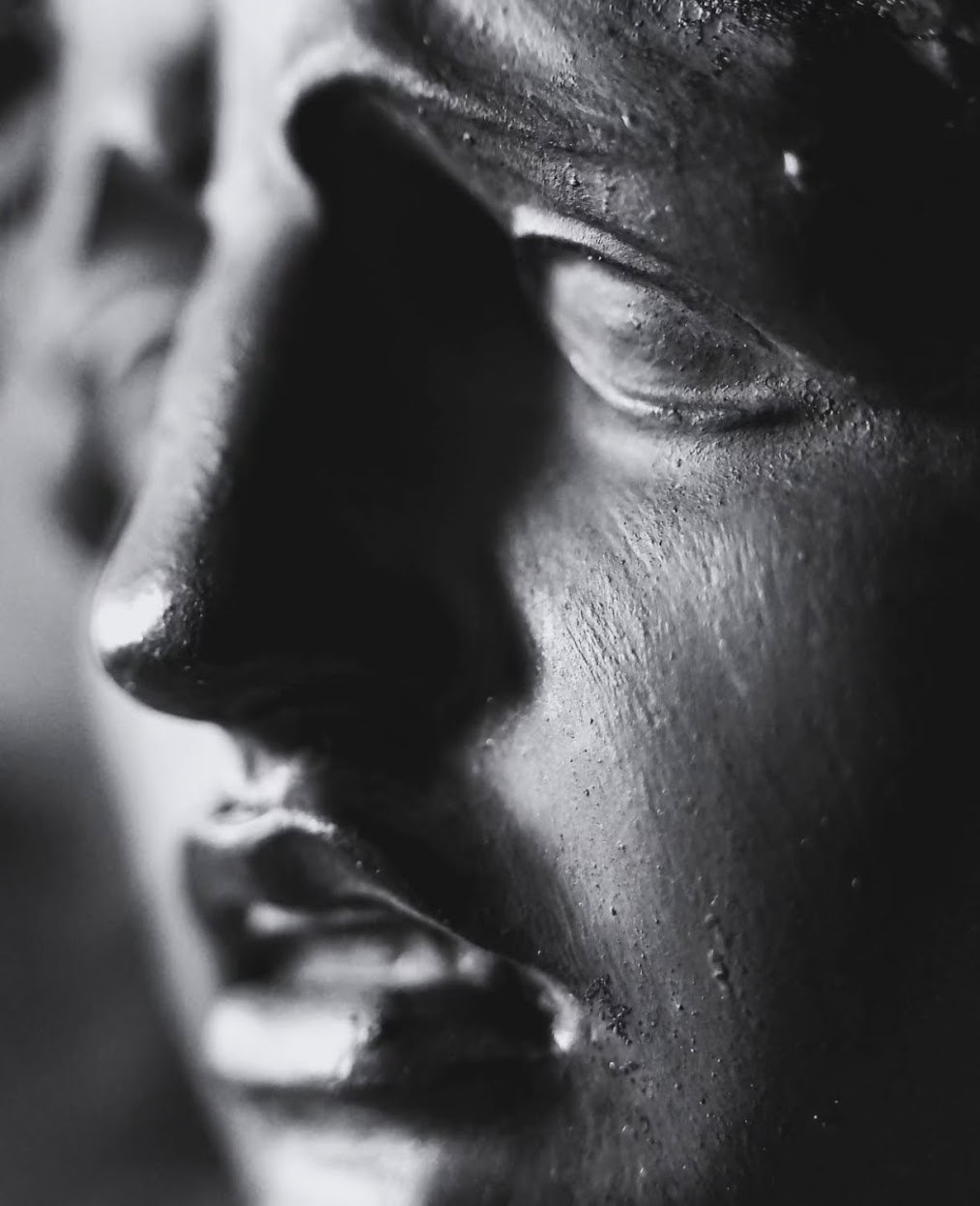 Detalle en blanco y negro de un rostro escultórico con textura visible y sombra suave.